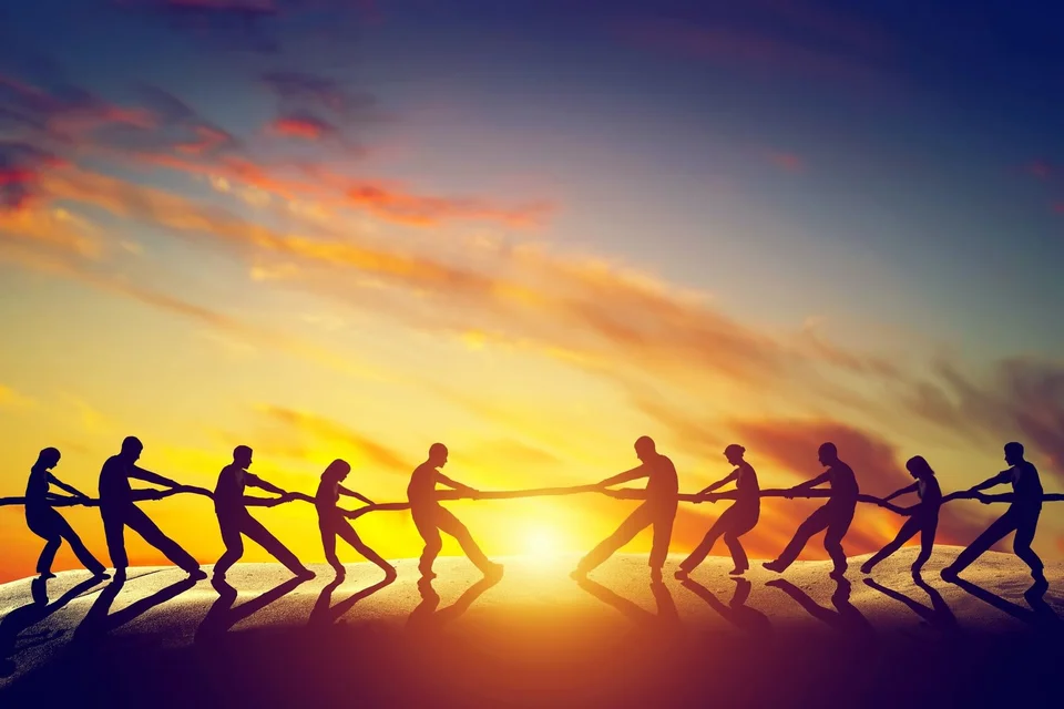 People playing tug o' war in front of a sunset