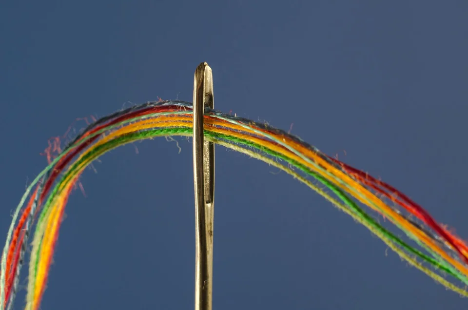 A multicolored thread being pulled through the eye of a needle